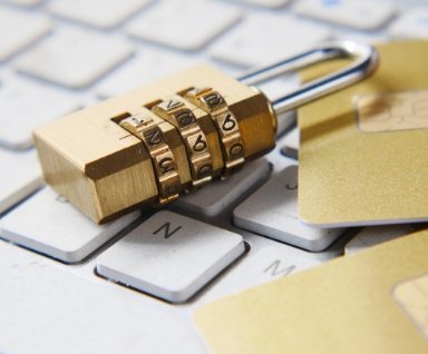 Brass combination padlock and a gold credit card resting on a white keyboard.